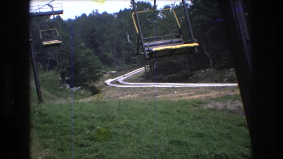 The final frame shows an empty chairlift seat crossing the foreground above a green slope, with a winding road and forested hillside behind it at Mt. Bromley.