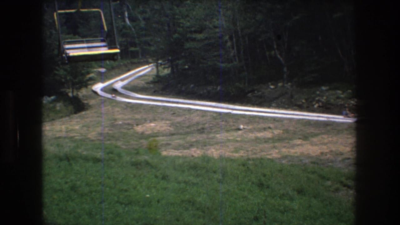 Chairlift seat and winding track seen from above near the forest edge.