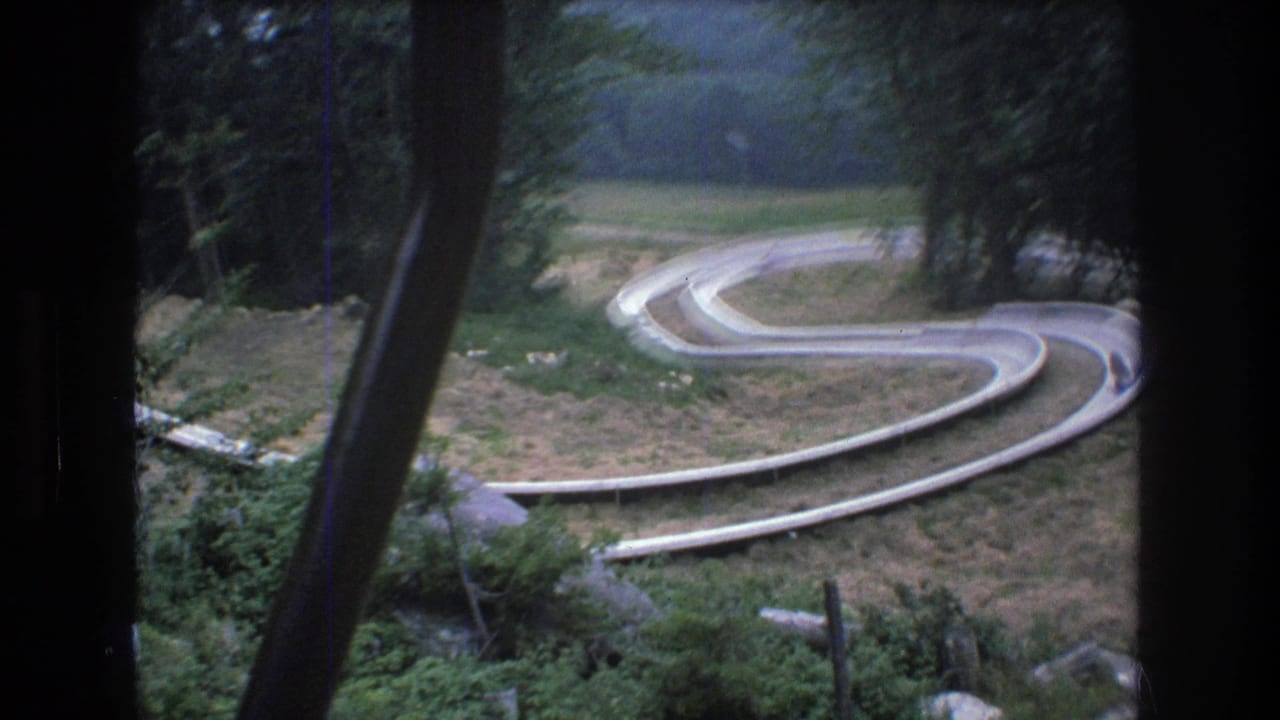 1976 8mm view from a chairlift at Mt. Bromley, Vermont, looking down toward a winding alpine slide track through a wooded hillside.