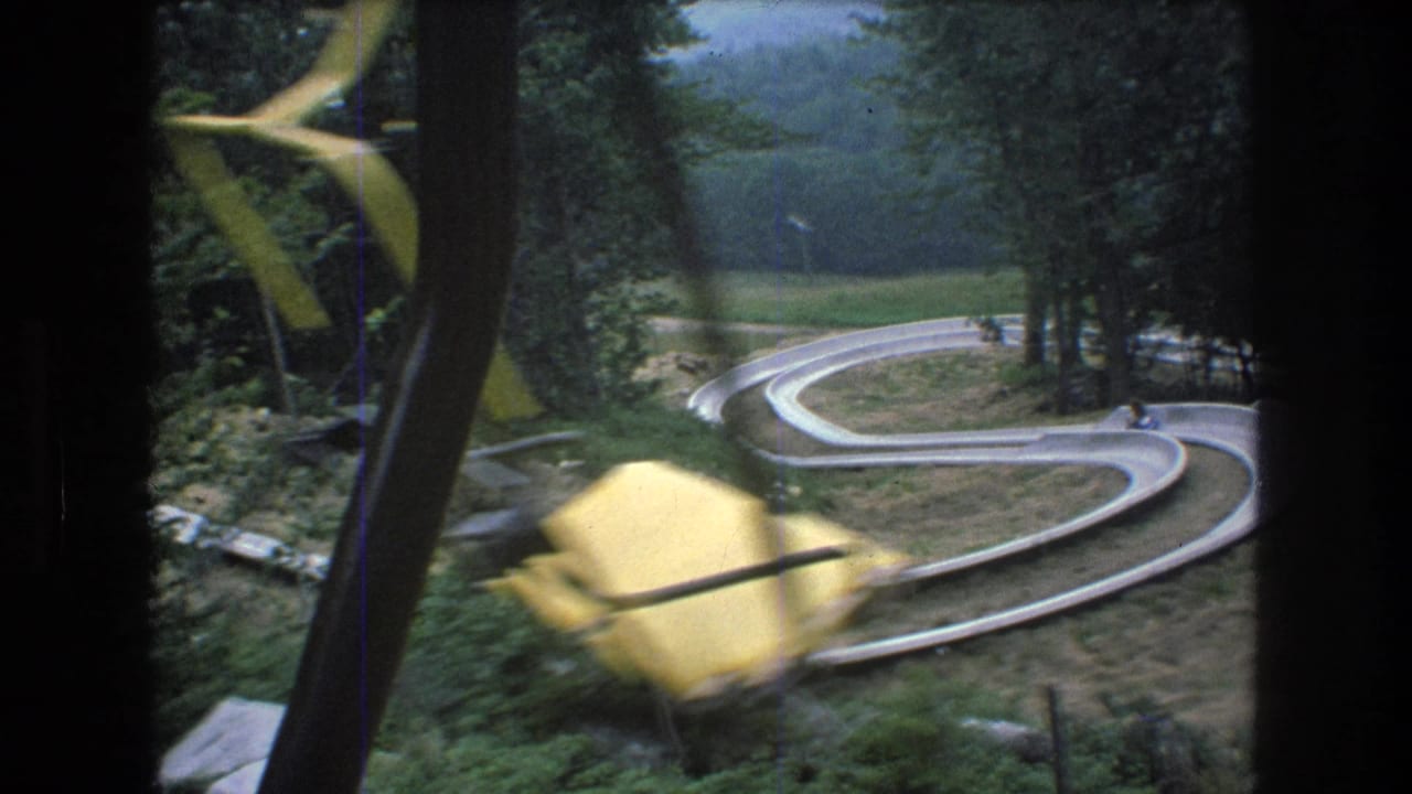 Yellow chairlift seat passing in front of a winding slide track.