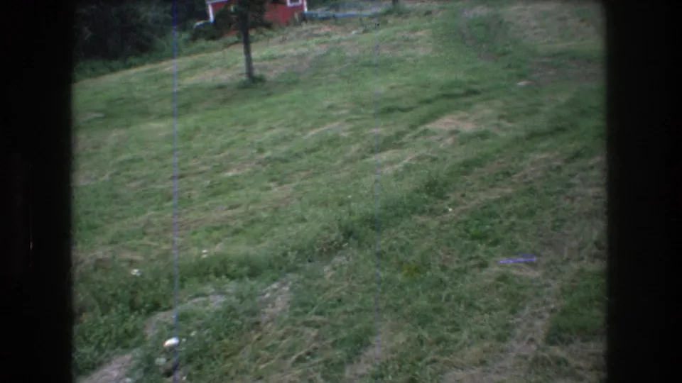 A moving 8mm view across the Mt. Bromley grassy ski slope, with a lift pole, red building, and worn paths visible in the frame.