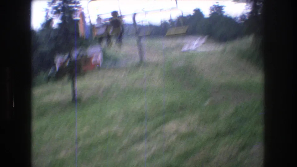 Motion-blurred 1976 Mt. Bromley chairlift frame with a rider silhouetted on the lift above the grassy summer hillside.