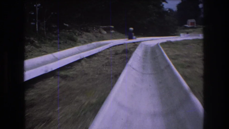 Near the end of the clip, the Mt. Bromley alpine slide curves through grass with another rider briefly visible ahead and the wooded slope beyond.