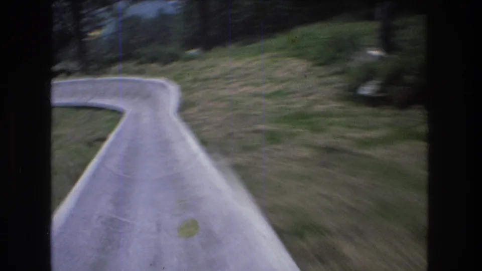 1976 Mt Bromley, Vermont 8mm frame with a forward-looking view along the alpine slide track as it curves through grass toward a wooded area.