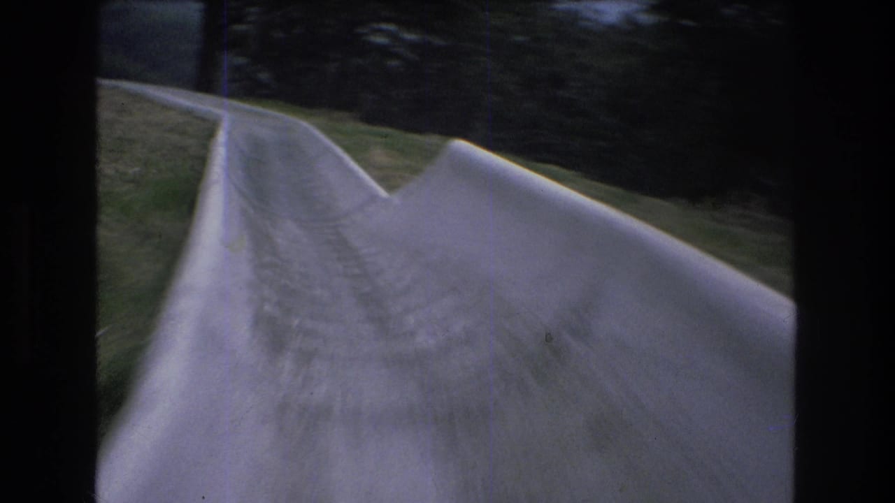 1976 8mm home-movie frame from Mt Bromley, Vermont, showing a point-of-view look down a pale concrete slide with raised sides, grass, and trees ahead.