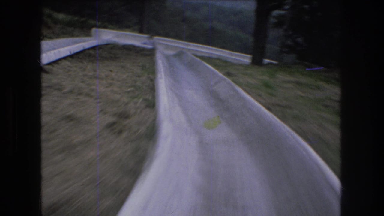 Curving concrete slide seen from a moving point of view with grass and trees nearby.