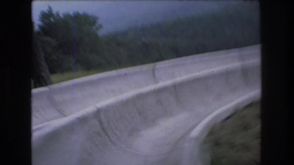 Late frame from the 1976 Mt Bromley slide POV, with the concrete side wall filling the foreground and wooded hills visible beyond the grassy slope.