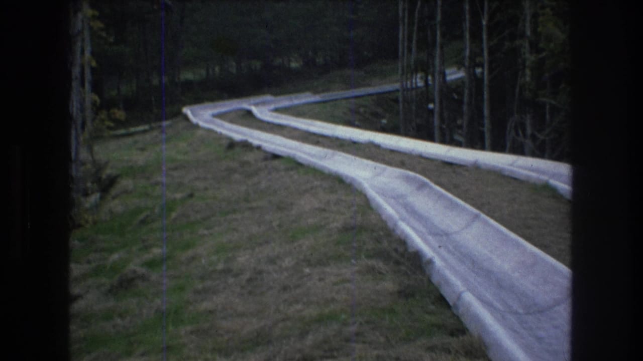 1976 Mt Bromley, Vermont 8mm frame showing an empty pale bobsled or luge-style track curving through a wooded hillside.
