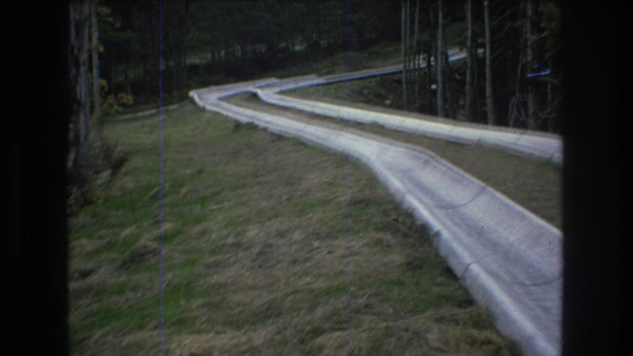 Curving concrete track runs through a forested hillside with dark film borders.