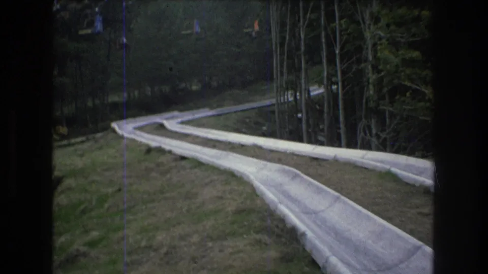 1976 Mt Bromley, Vermont 8mm frame showing the empty resort track receding across grass and trees, with small distant slope features visible.