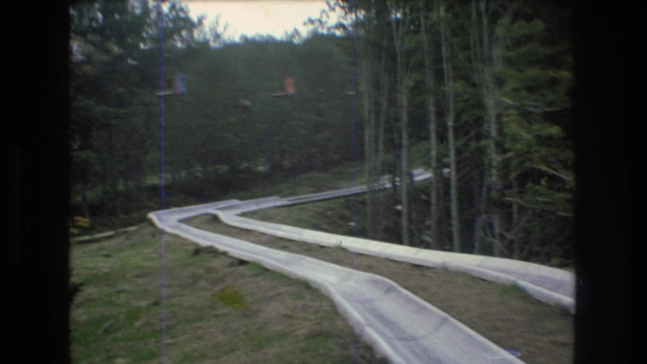 1976 Mt. Bromley, Vermont 8mm frame showing a pale alpine slide track bending downhill through grass and dense trees.