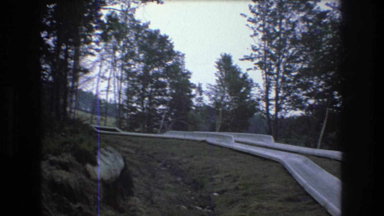 1976 Mt Bromley, Vermont 8mm frame showing pale concrete slide lanes winding across grass and earth among trees on a wooded slope.