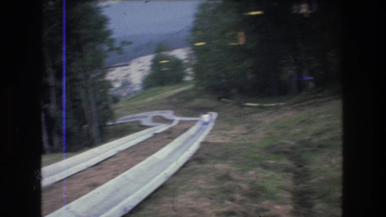 Supported by the clip metadata, this 1976 Mt Bromley, Vermont frame shows a white alpine slide descending through trees and grass with a small distant person near the slide.