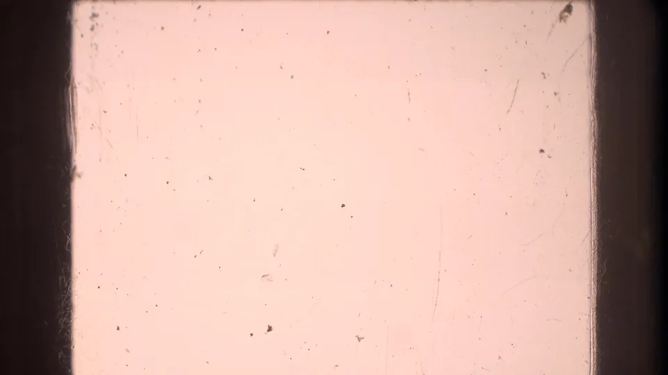 A mostly pink-tinted 8mm frame with dark gate edges, dust, scratches, and little recognizable scene detail visible.