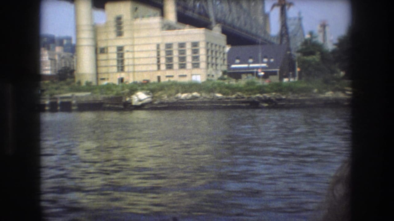 Industrial waterfront building beside murky river water under a steel bridge.