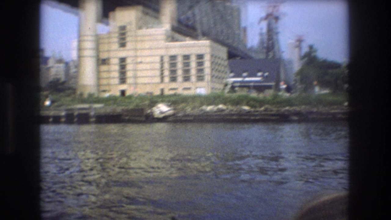 Riverfront industrial building and small boat seen below a steel bridge.