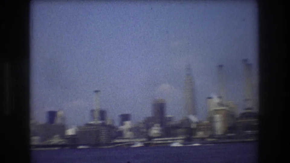 Soft, hazy 1976 New York City skyline from the water, with distant buildings and boats rendered in grainy 8mm color.