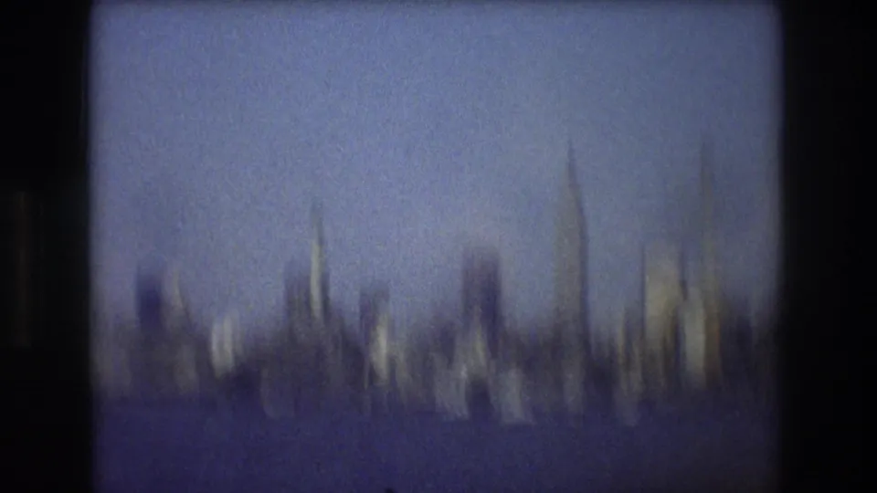 A motion-blurred 1976 New York City skyline is filmed from the water, with buildings and stacks smeared by boat movement and handheld camera shake.