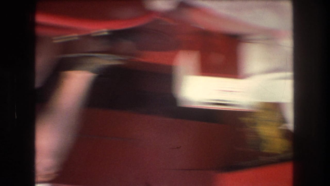 Blurred 1976 8mm home-movie frame showing a red boat interior or surface with dark and pale shapes as the camera spins during a boat ride.
