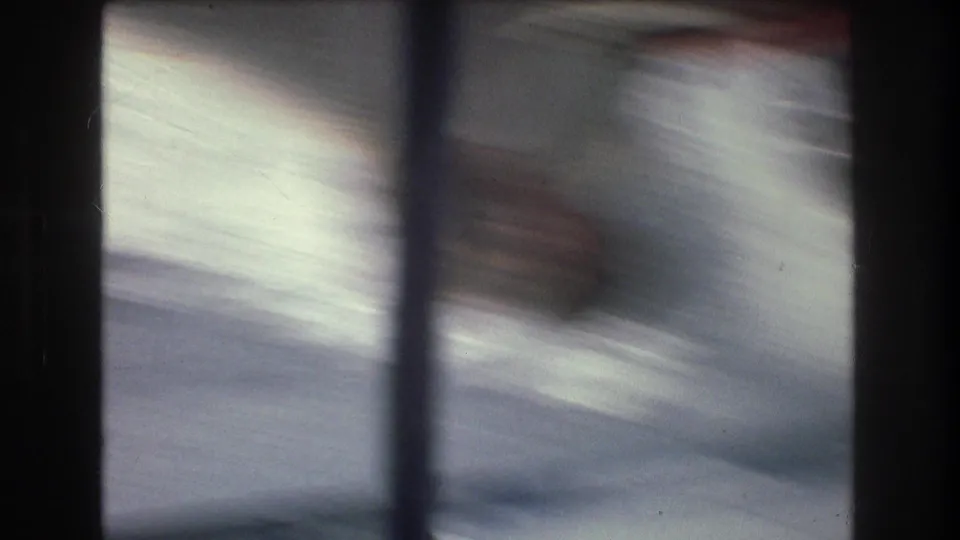 Heavily blurred 8mm frame from the boat ride, with blue-gray water tones, vertical dark streaks, and the physical film-frame border visible.