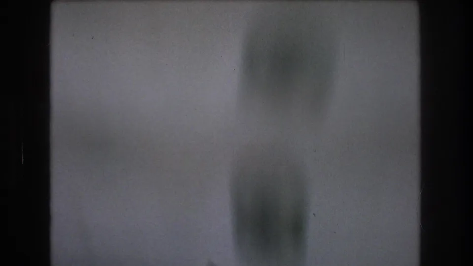 Soft, gray-blue 8mm home-movie frame with indistinct vertical forms and heavy blur as the boat-camera view continues spinning or tilting.