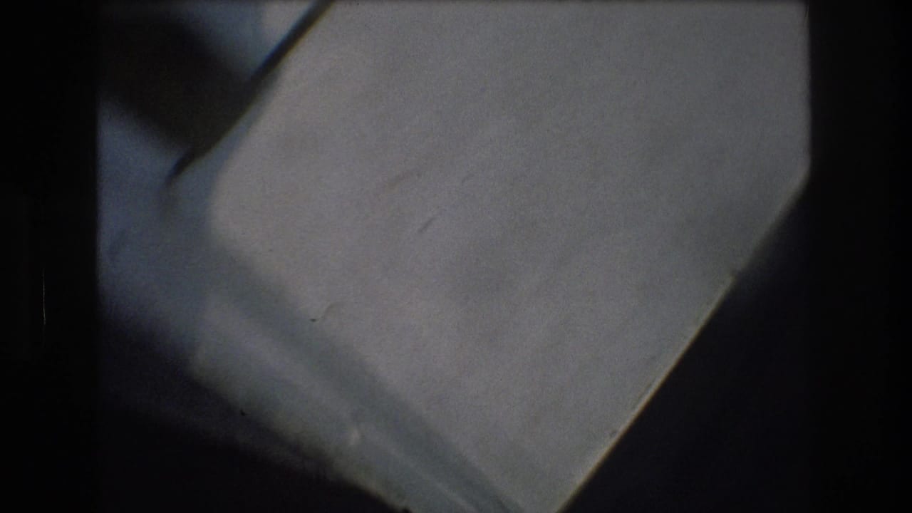 Soft 1976 8mm frame from New York City showing pale indoor surfaces, diagonal edges, shadow, and dark film borders during unstable camera movement.