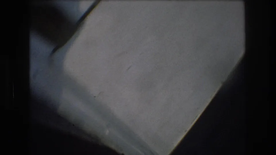 Soft 1976 8mm frame from New York City showing pale indoor surfaces, diagonal edges, shadow, and dark film borders during unstable camera movement.