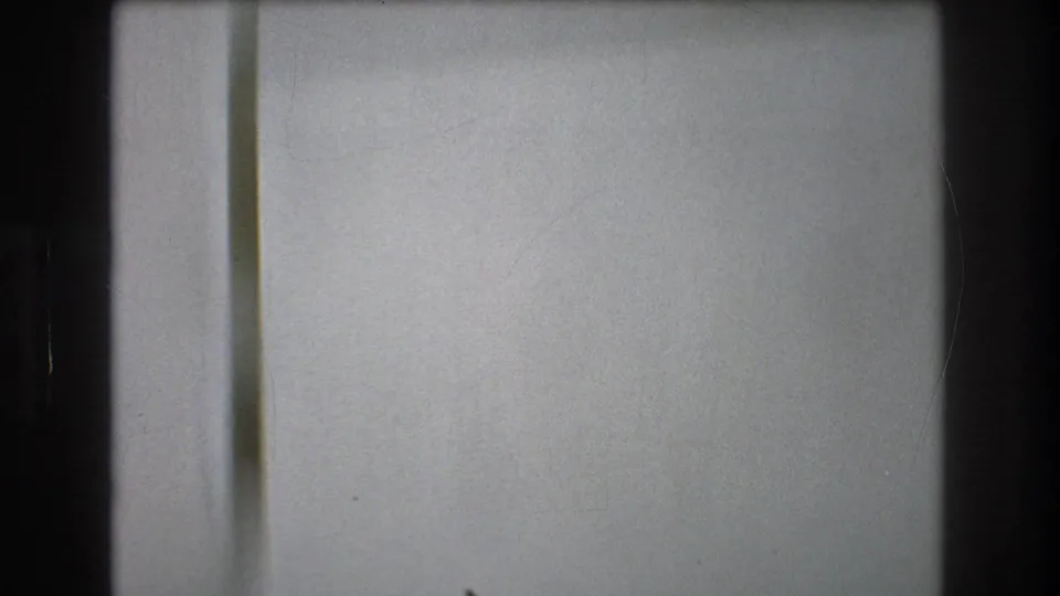 Plain pale wall or floor surface in a 1976 New York City 8mm frame, with a narrow vertical edge, dark border, and soft scanned-film texture.