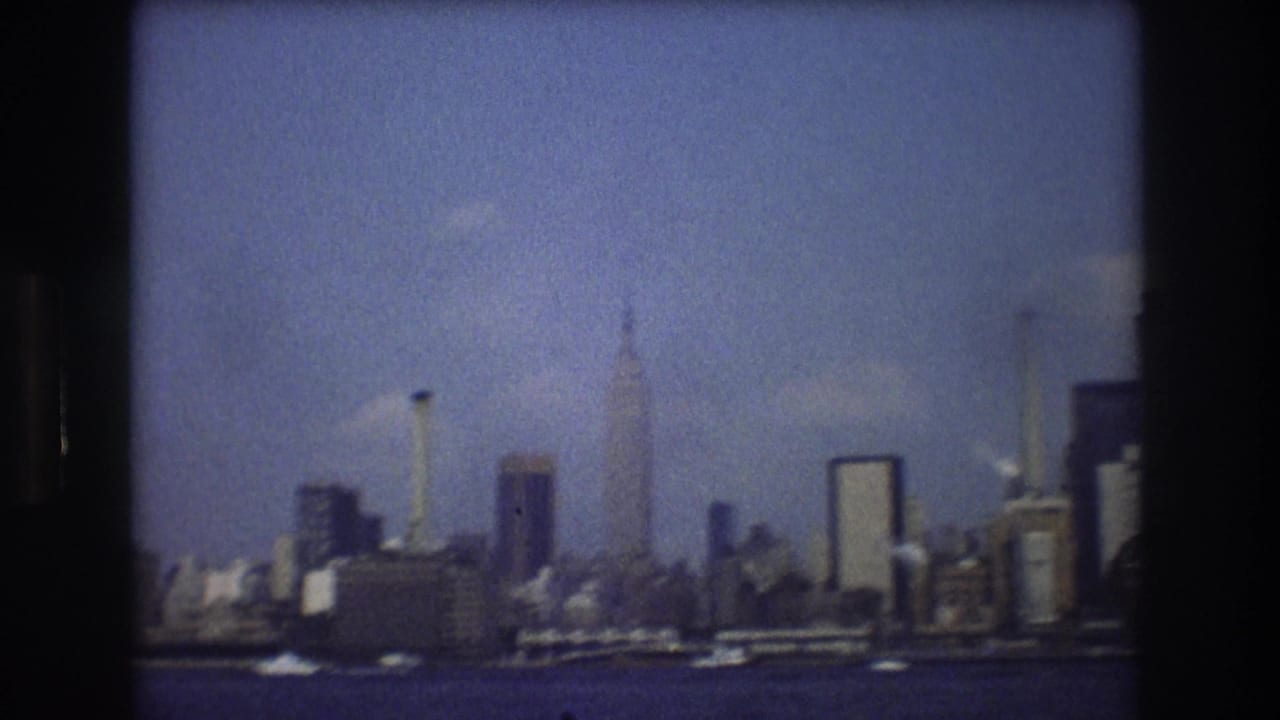 Soft 8mm frame of the New York City skyline from a moving boat, with the Empire State Building and other tall buildings visible beyond the water.