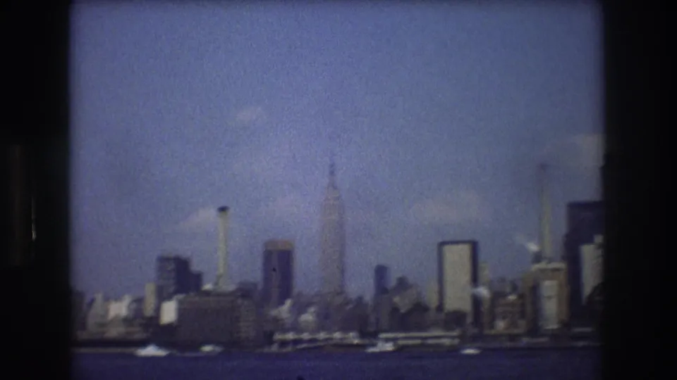 Soft 8mm frame of the New York City skyline from a moving boat, with the Empire State Building and other tall buildings visible beyond the water.