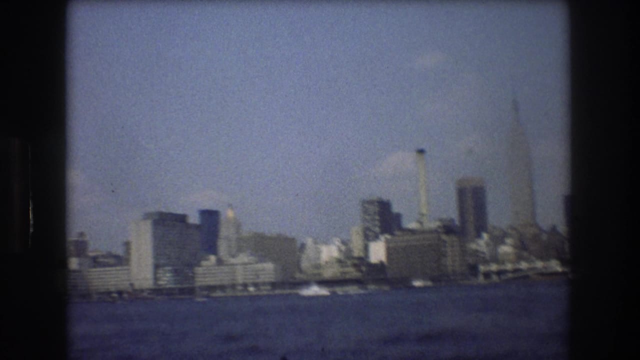 Distant Manhattan skyline across water with dark film-frame borders.