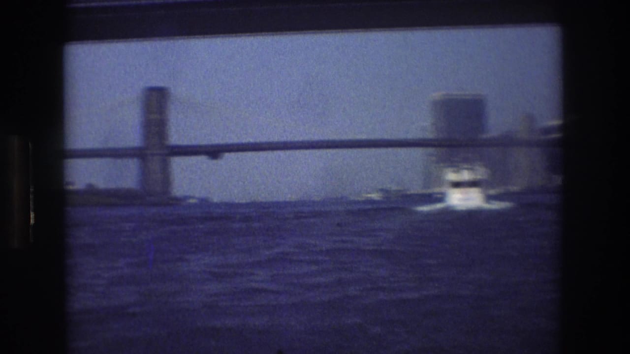 1976 New York City 8mm boat-view frame showing rippled water, a bridge structure, and a small motorboat moving ahead in soft focus.