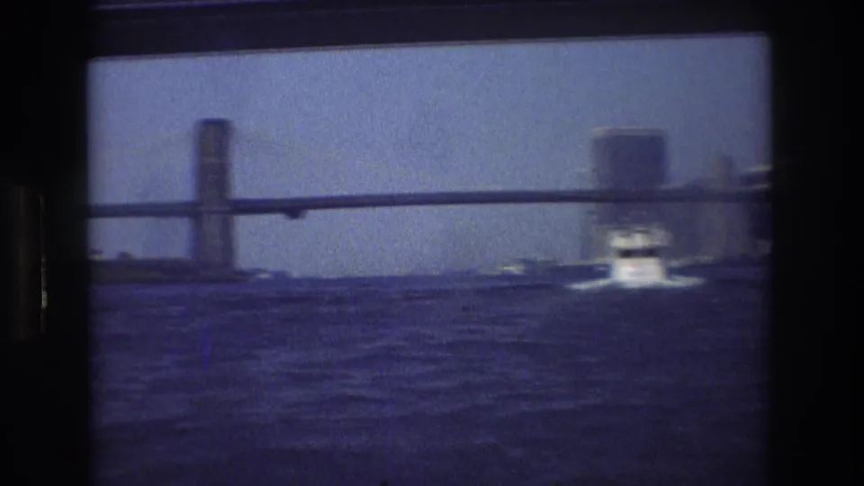 1976 New York City 8mm boat-view frame showing rippled water, a bridge structure, and a small motorboat moving ahead in soft focus.