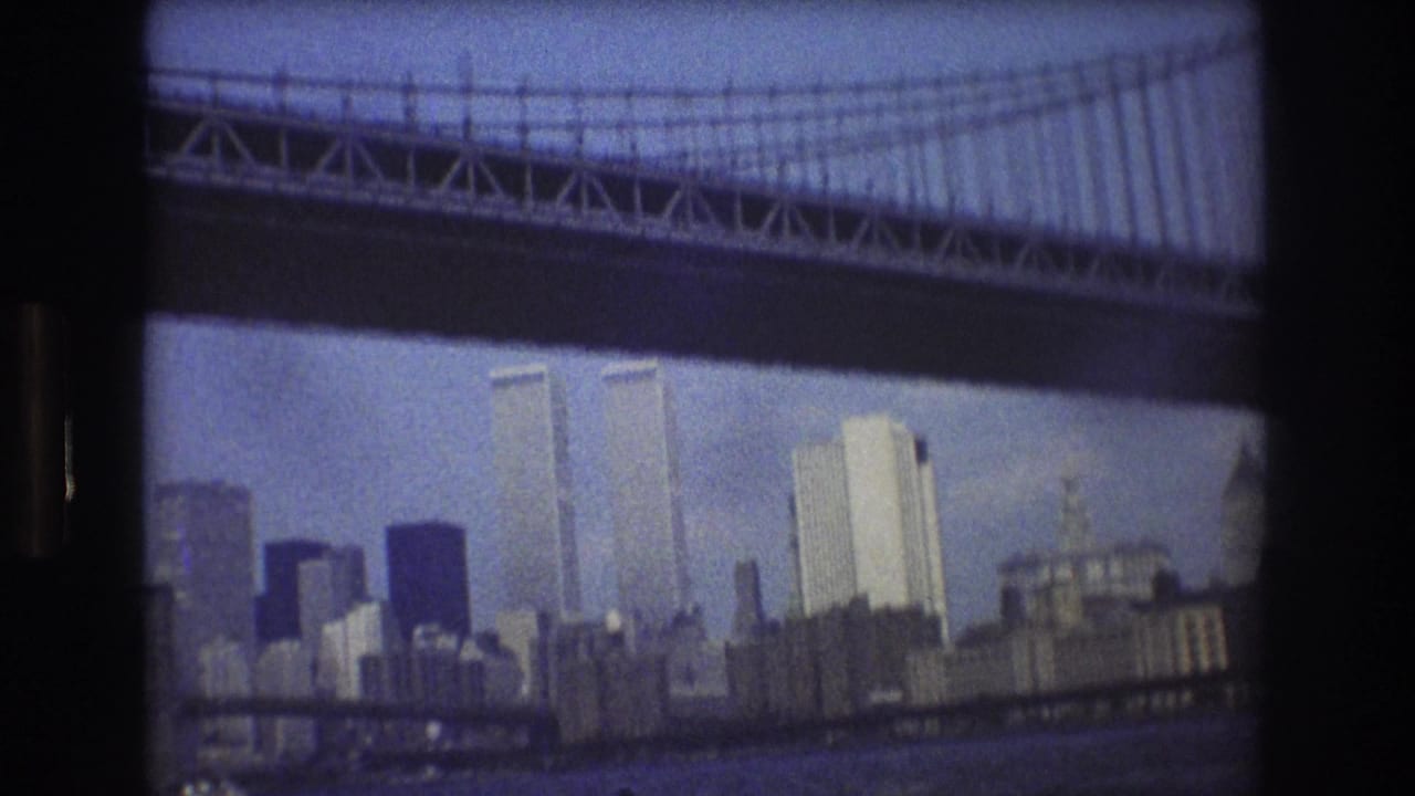 1976 8mm view of New York City's Manhattan skyline, with the Twin Towers visible below the dark underside of a large suspension bridge.