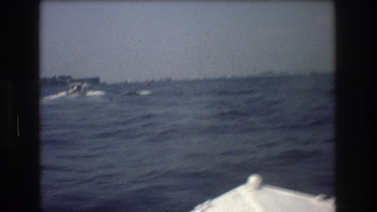 1976 8mm home-movie frame from near New York City showing a white boat bow at the bottom of the frame and rough open water stretching to a low horizon.
