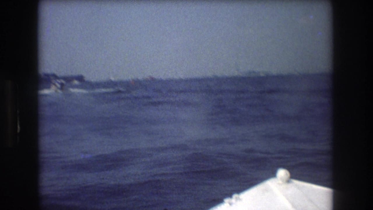 Boat bow at lower right with open water and distant small craft or shoreline on the horizon.
