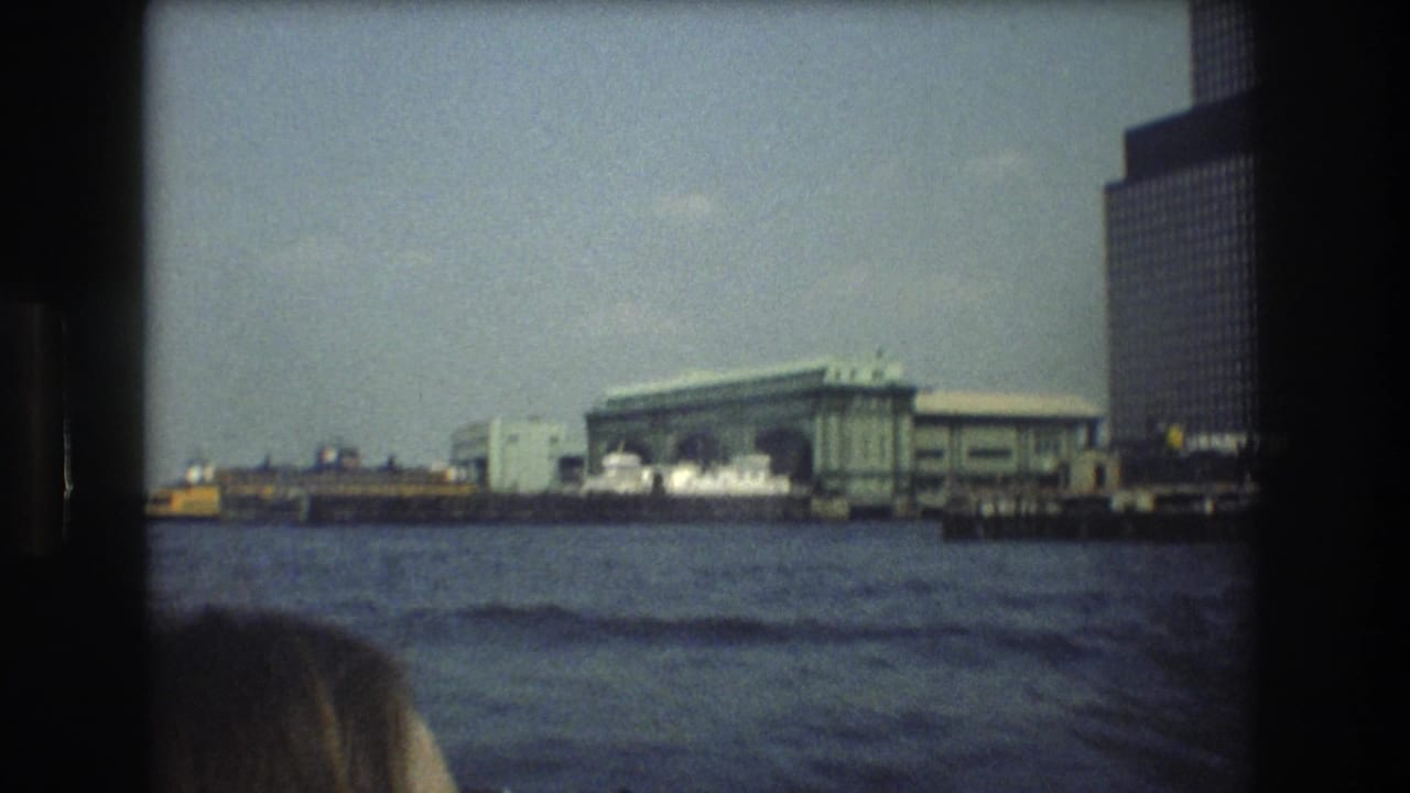 New York City harbor scene from the supplied 1976 footage, with a terminal across the water, modern high-rise buildings, and a partial passenger head in the foreground.