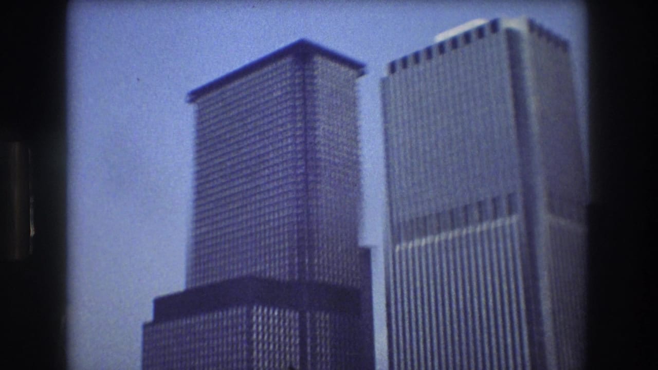 1976 8mm home-movie view of Lower Manhattan skyscrapers from the water, with tall office towers framed by dark film edges.