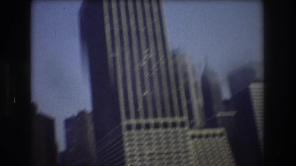 1976 8mm view of a tall New York City tower and surrounding skyline elements, slightly blurred by handheld movement from the water.
