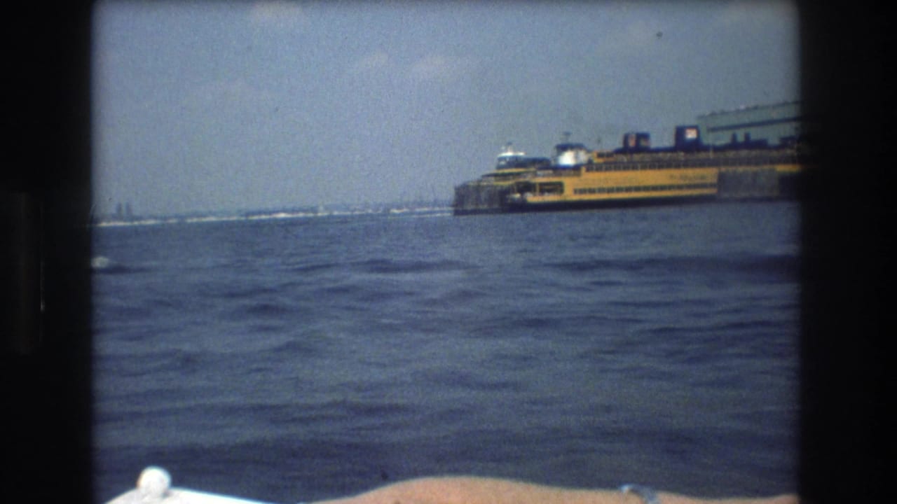 Distant yellow ferry on harbor water with a boat rail and passenger arm at the lower edge.
