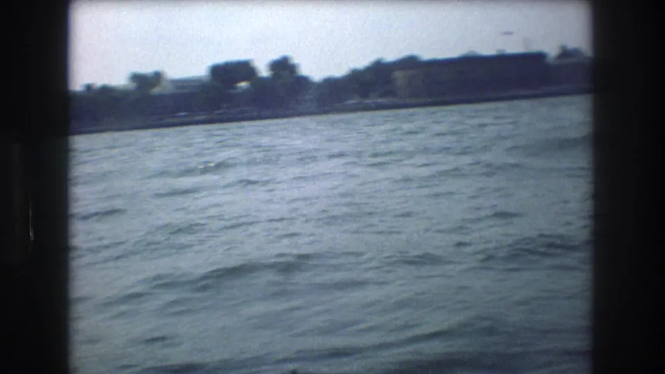 1976 New York City boat-view frame looking over rippled harbor water toward a soft, distant shoreline after the ferry has moved out of the main view.