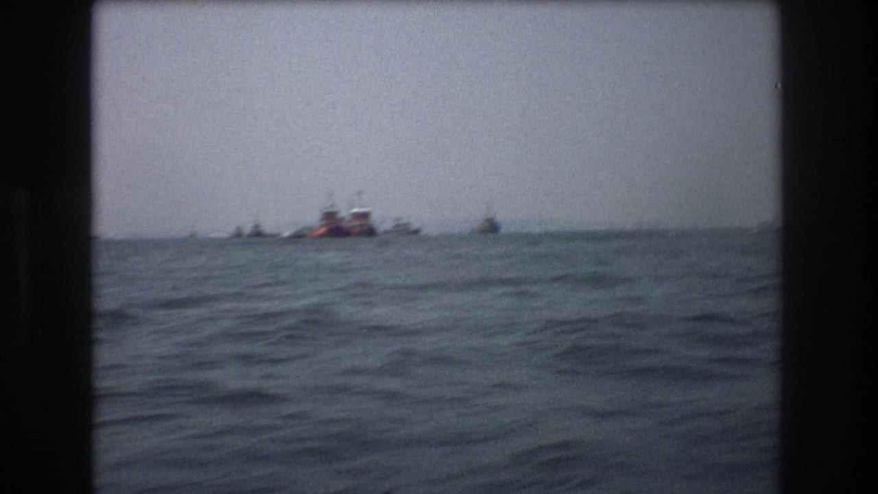 Water-level 8mm frame from the documented 1976 New York City clip, with small distant boats and a red vessel beyond rolling waves.