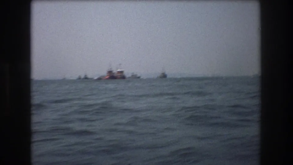 Water-level 8mm frame from the documented 1976 New York City clip, with small distant boats and a red vessel beyond rolling waves.