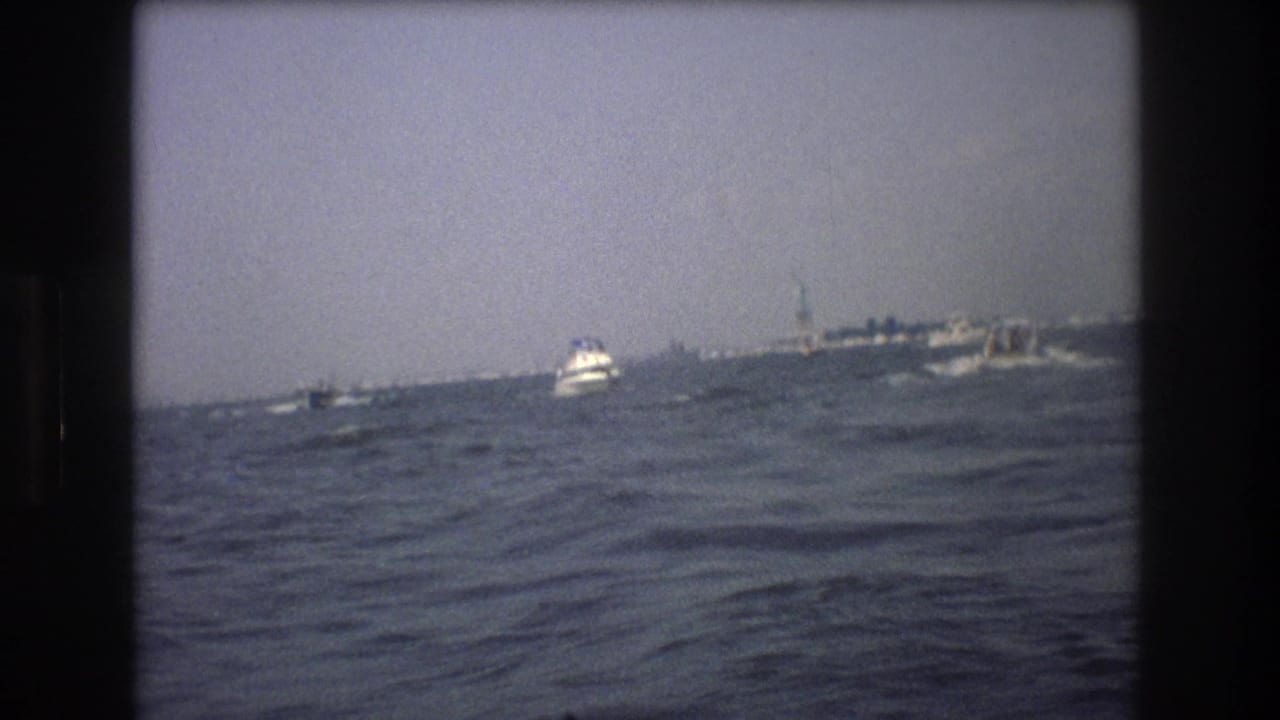 Small white boat on choppy water with distant vessel or pier on the horizon.