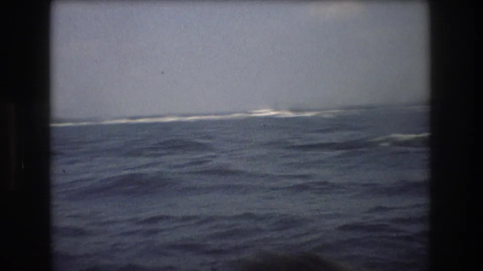 Wide 1976 New York City harbor view showing rough water, distant white wakes, and a pale hazy sky with no visible people.