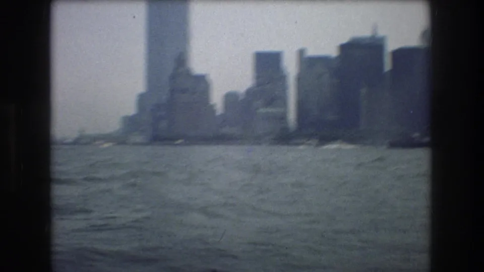 1976 8mm New York City harbor view with distant skyline forms across choppy water under a pale, hazy sky.