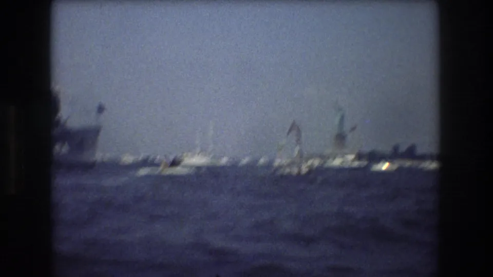Small sailboats and harbor vessels move across New York Harbor in soft, hazy 1970s 8mm footage.