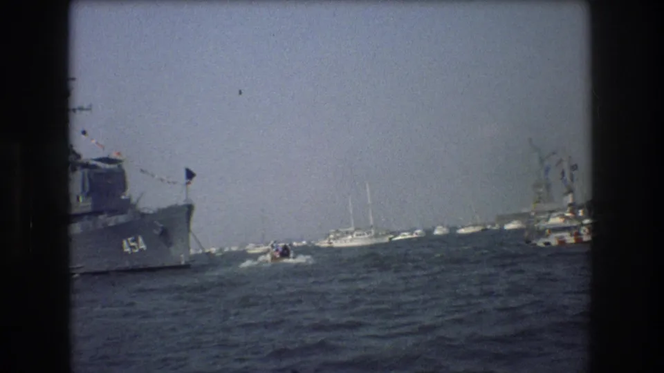 1976 New York Harbor view with a naval vessel marked 454, small boats, sailboats, and the Statue of Liberty beyond the water.