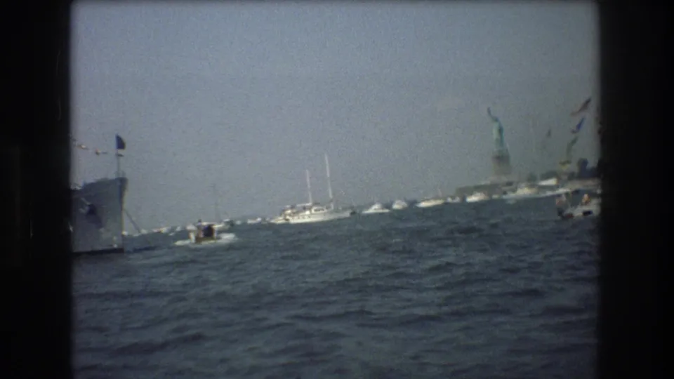 1976 harbor frame showing small boats and sailboats on the water, with the Statue of Liberty visible near the right side of the frame.