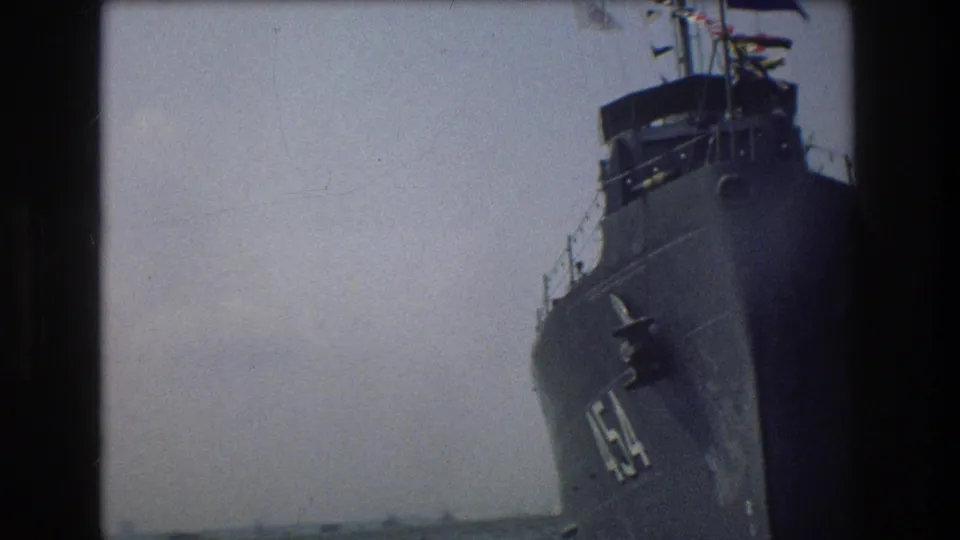 The bow and forward side of a large dark Navy vessel fill the frame, with partial white hull numbering visible against a pale sky.